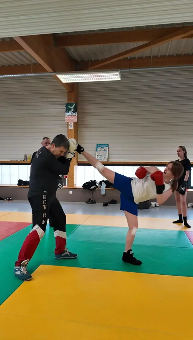 Une boxeuse porte un coup de pied dans les gants d’un entraîneur.